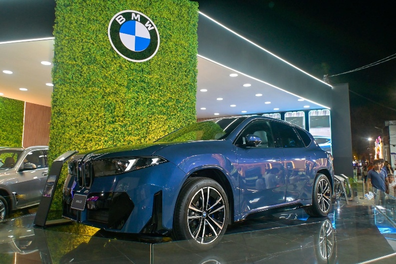Automóvil BMW azul en el showroom, junto a la pared verde con el logo BMW